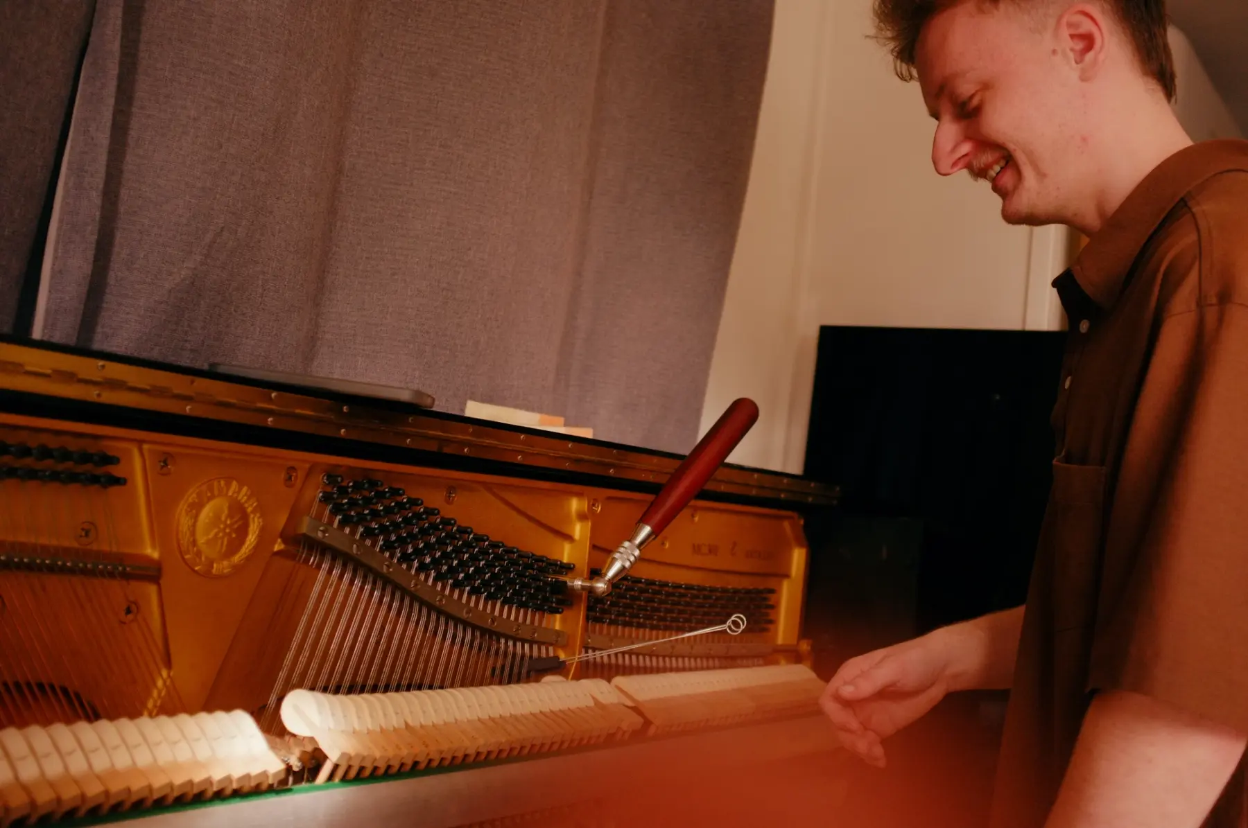 Reuben smiling while inspecting the action of an upright piano